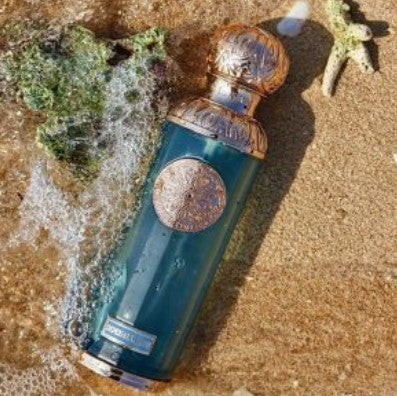 Blue glass perfume bottle with gold cap and round decorative label, lying on sand