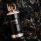Black perfume extrait bottle with gold cap, gold logo label, and textured base ring