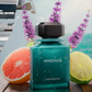 Teal perfume bottle with dark cap, MYKONOS label, citrus slices nearby