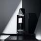 Black eau de parfum bottle with faceted top, UNE label on stand